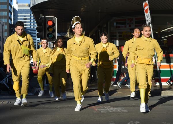 A group of young people, crossing a street in yellow jump suits