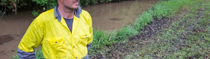 Australian farmer wearing high visibility clothing on his farm while inspecting damage from a flooded creek