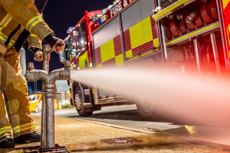 Photo of a fire fighter next to a fire engine, opening a hydrate.