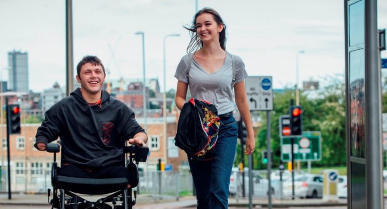 Man in electric wheelchair walking down city street with young woman
