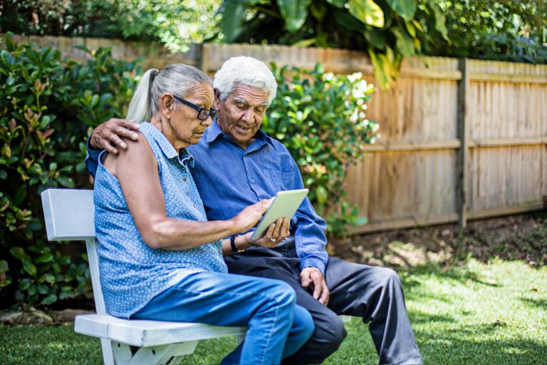 Senior couple sitting in a garden on a tablet. 