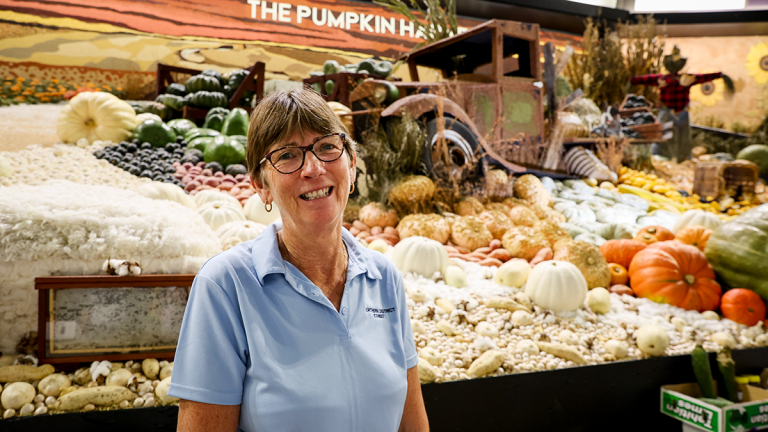 Smiling volunteer woman standing in front of a display of fresh vegetables