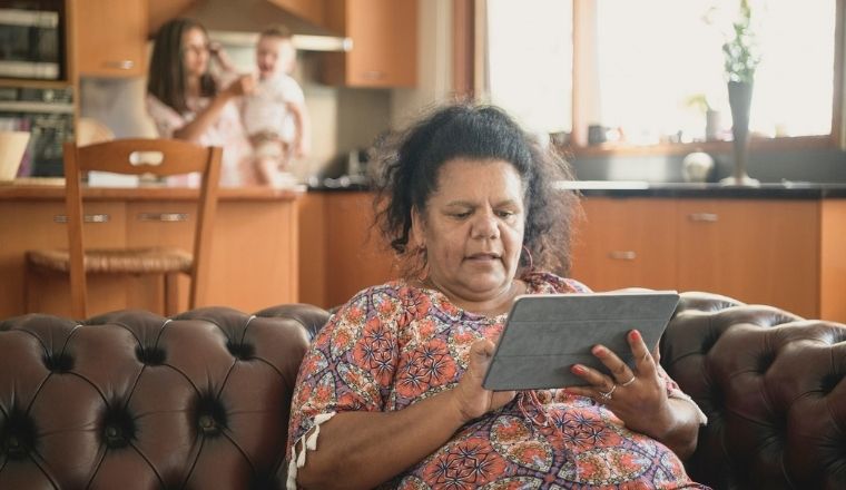 A lady sitting on her couch in her loungeroom, scrolling through her tablet.