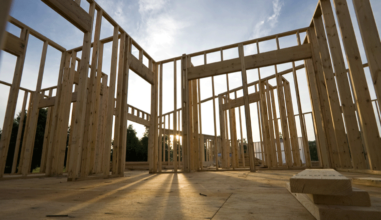 A partially completed house frame stands as the sun slowly sets in the background