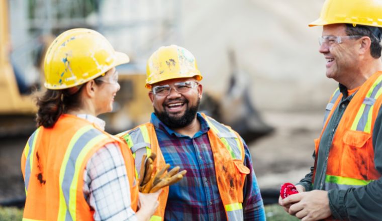 A group of 3 construction workers in PPE having a conversation and smiling. 