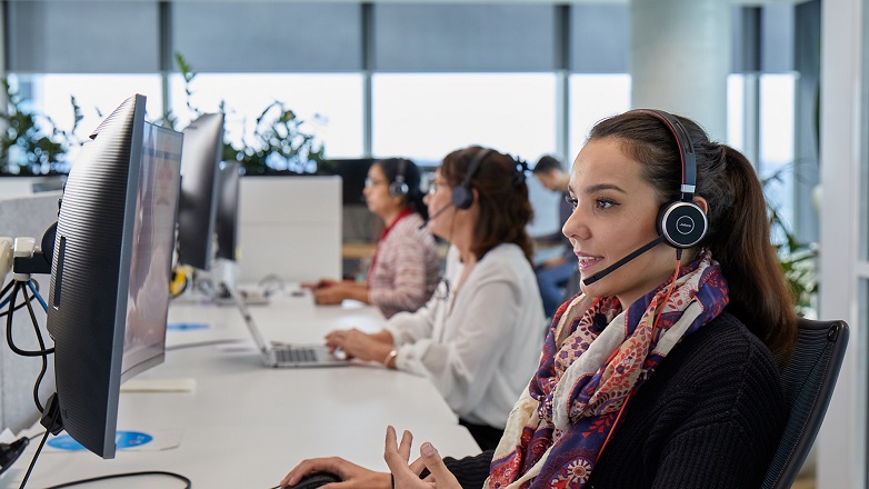 A woman call centre operator sitting at a desk, in a phone call. Two other women call centre operators are sitting in the same row.