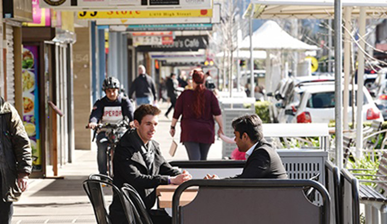 Two men in cafe talking outside with cyclist in background in the high street