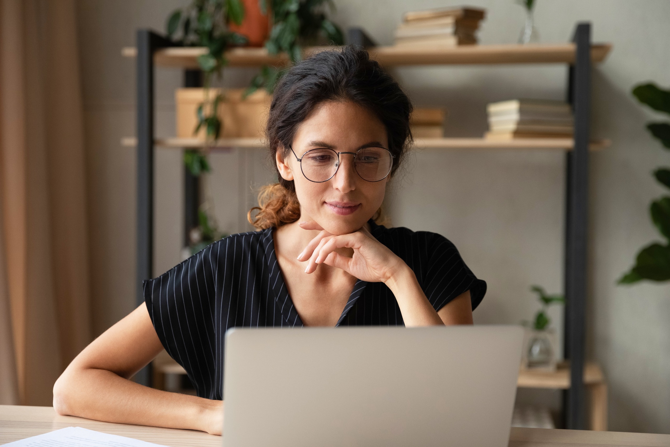 A girl wearing glasses sitting at a table working on a laptop