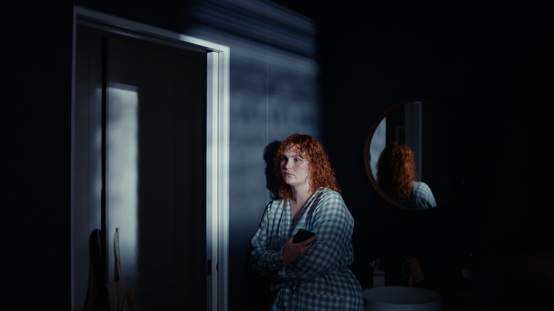 A woman with red hair standing in a dark room against a wall