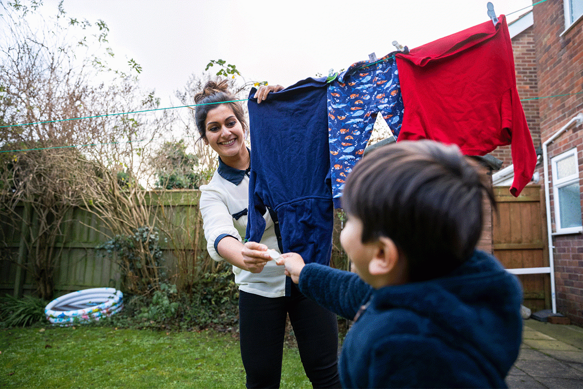 A mother and her son are hanging washing up on a clothes line in their backyard.