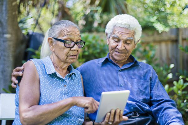 Male and female elderly Aboriginal couple reading iPad in back yard