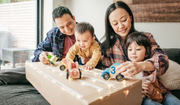 A father, baby, mother and toddler all play together around a coffee table