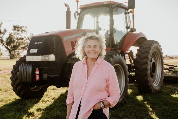 Woman wearing pink button up shirt with hand in pocket smiling and standing in front of a red tractor