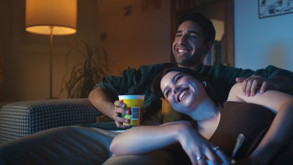 A couple on a couch smiling and watching tv