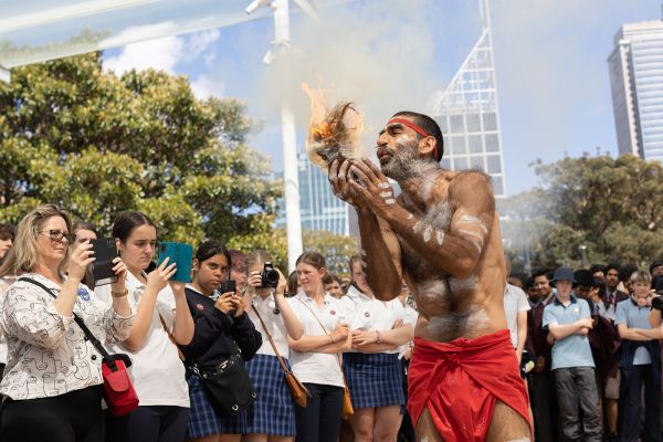 Art Gallery New South Wales School Day. Aboriginal man blowing fire in his hand whilst students and teachers watch outside