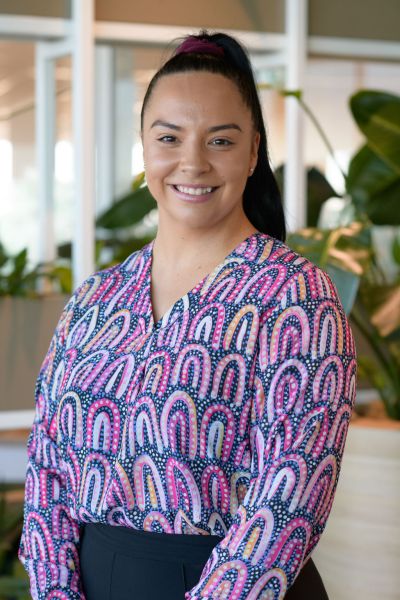 A woman is standing in a corporate office wearing a colourful blouse with an indigenous print.
