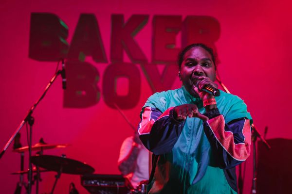 BakerBoy performing on stage lit with pink lighting and his name in the background.