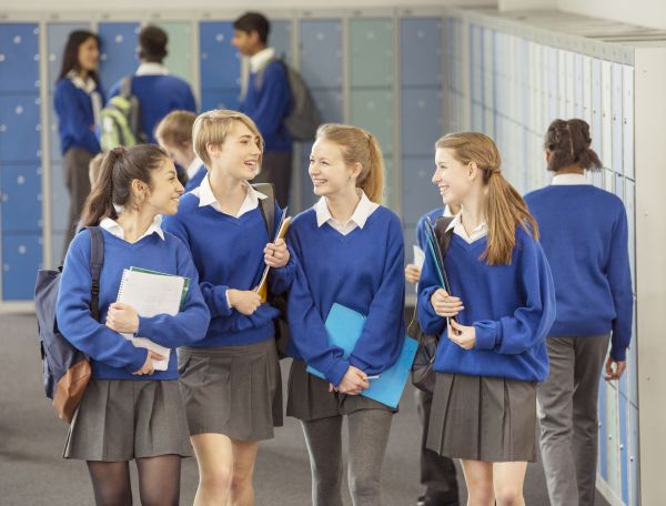 A group of school students in school uniform talking and smiling at each other as they walk.