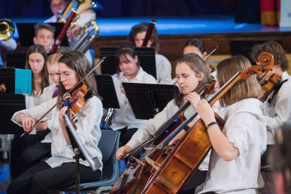 Image of an orchestra who are all young people, playing various string instruments.