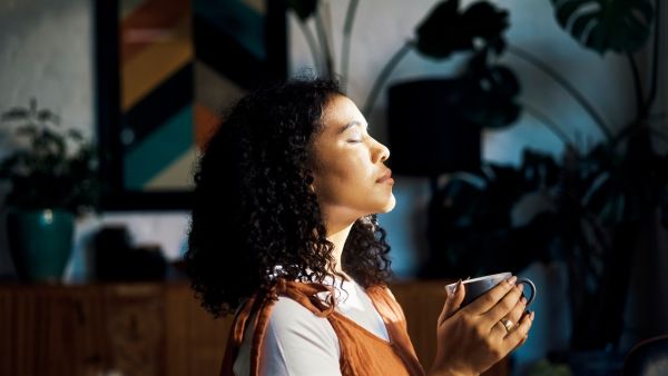 Woman drinking a drink and meditating in her home with her eyes closed