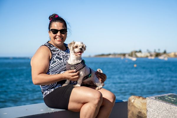 Woman sitting by the water smiling and holding a dog