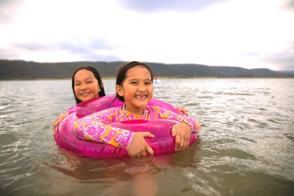 Two girls swimming in a large body of water. One girl is in an inflatable doughnut