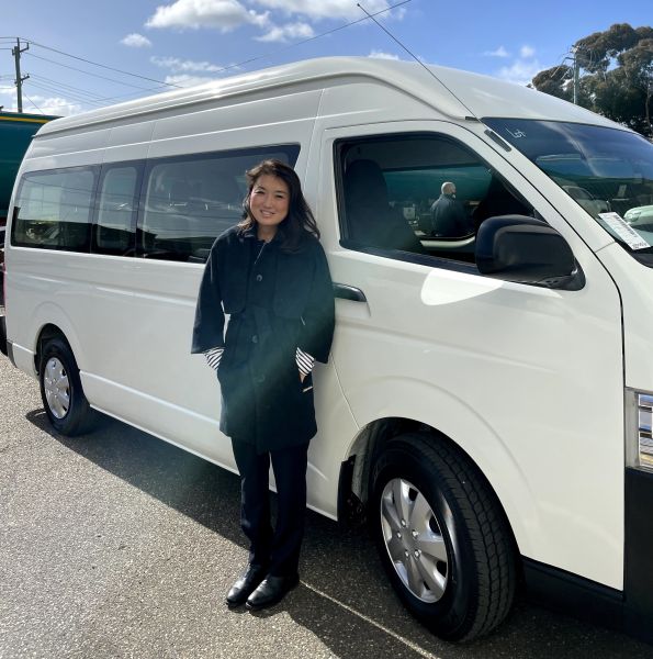 Young woman dressed in black coat stands in front of a white van