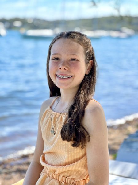 Young girl stands by the ocean in a dress smiling at the camera