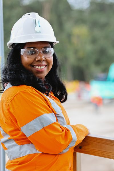 A woman is standing on a construction site smiling at the camera