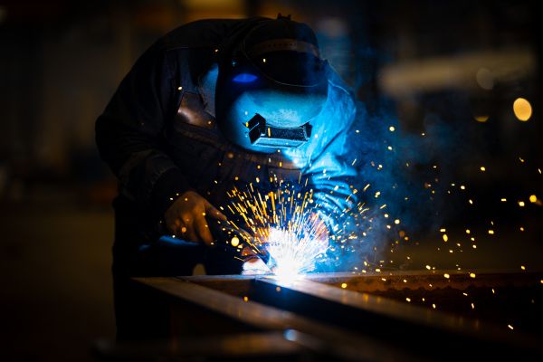 A welder, mask illuminated by a blue glow, sends orange sparks flying as he works.