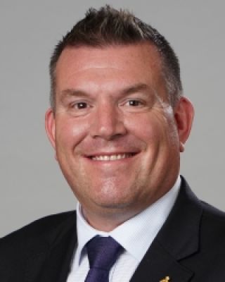 A picture of Minister Dugald Saunders wearing a suit smiling at the camera with a grey background