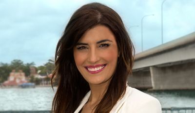 Eleni Petinos standing in front of a waterway and bridge in a white jacket