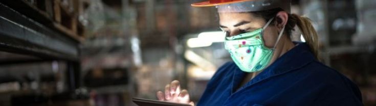 A woman wearing a face mask using a digital tablet