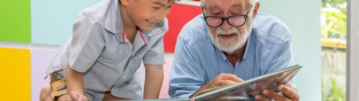 Older man wearing glasses reading a picture book with a child