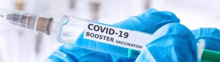 A gloved medical staff member holds a syringe containing a COVID-19 booster vaccination