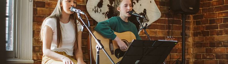 Two young female musicians performing at an indoor venue