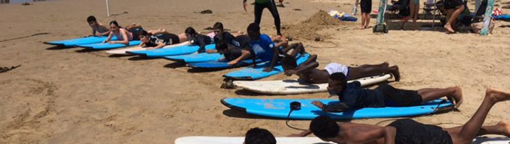 Young people laying on their surf boards at a beach with an instructor