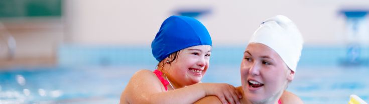 Young girl with Down's syndrome follows a swimming lesson with a coach