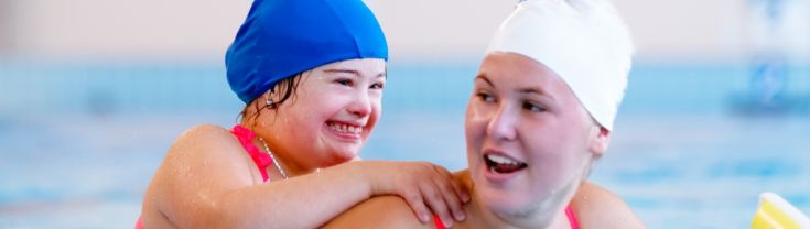 Young  girl with Young girl Downs Syndrome in swimming pool holding shoulder of instructor