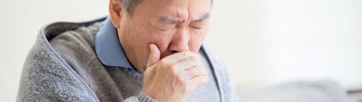 Man with blanket around his shoulders coughing on a couch