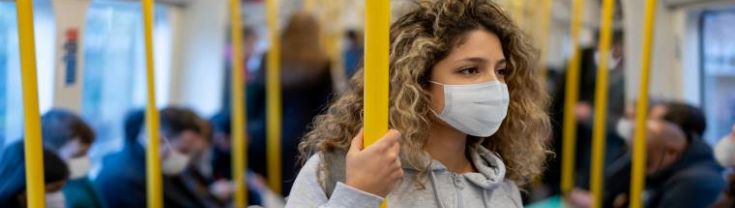 A young woman wears a face mask while standing on public transport.