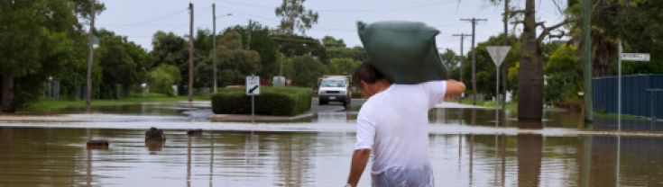 Man wading through floodwaters with esky and bag