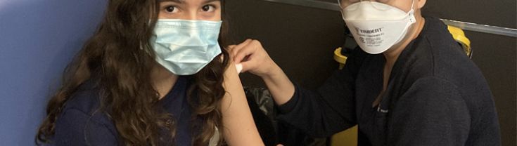 Young woman wearing mask gets needle in arm from a staff member