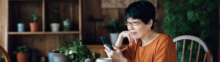Image of older lady sitting at dining table using mobile phone