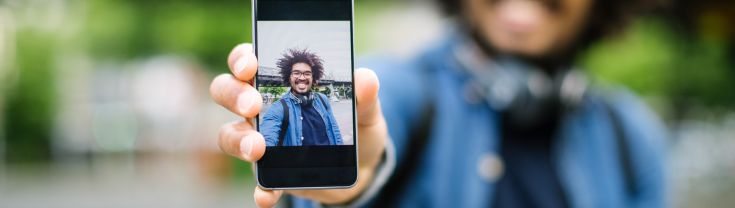 Image of young man holding phone out to show photo of himself