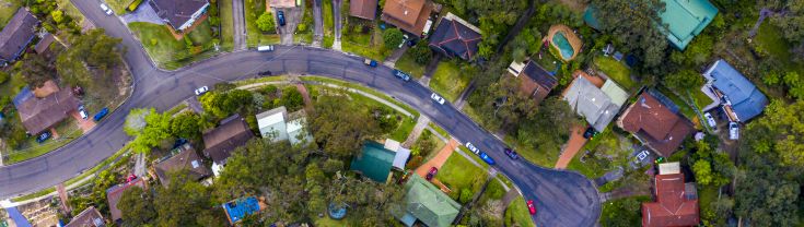 Birdseye view of a street of homes with pools in regional NSW with lots of trees and wide tarmac roads