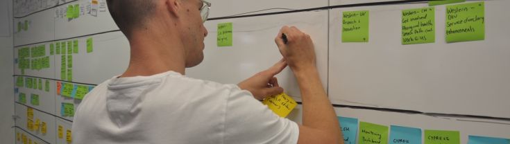 Man writing on a post-it note, stuck on a large whiteboard