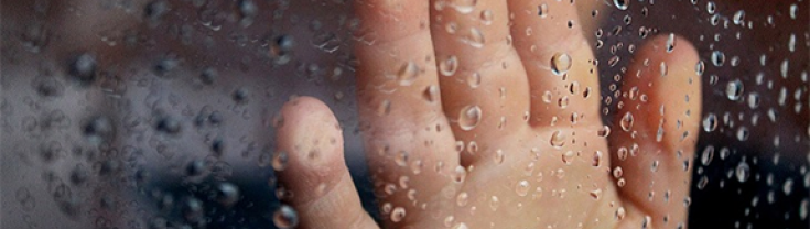 Hand on clear glass with rain drops on it
