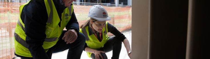 Two NSW Government building inspectors in high visibility yellow vests and white hard hats inspecting an apartment during construction.