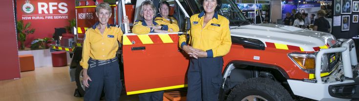 4 women wearing fire fighting ppe, standing with a small firetruck